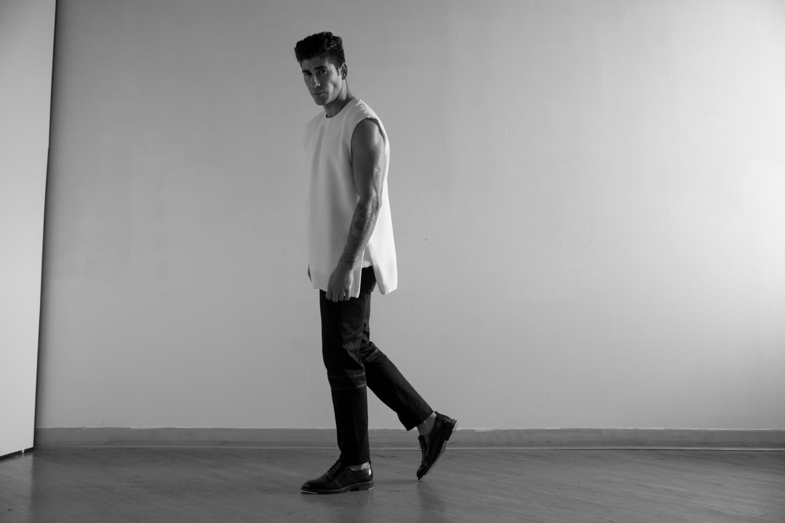 Black-and-white studio look: sleeveless white tunic, dark trousers, mid-stride.